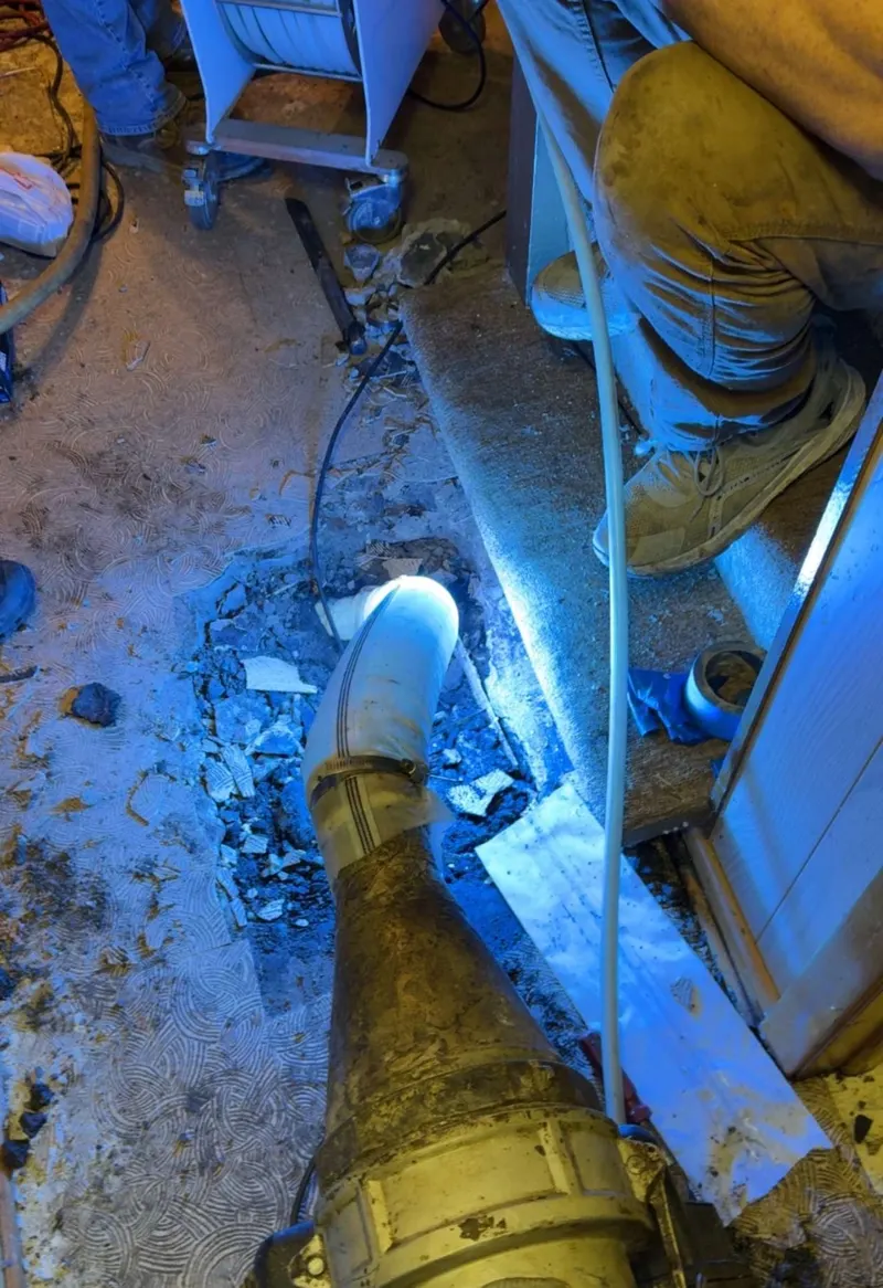 Crew working a drain line indoors with a camera reel and liner equipment